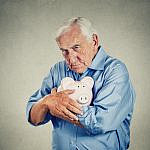 Senior man holding piggy bank isolated on gray wall background